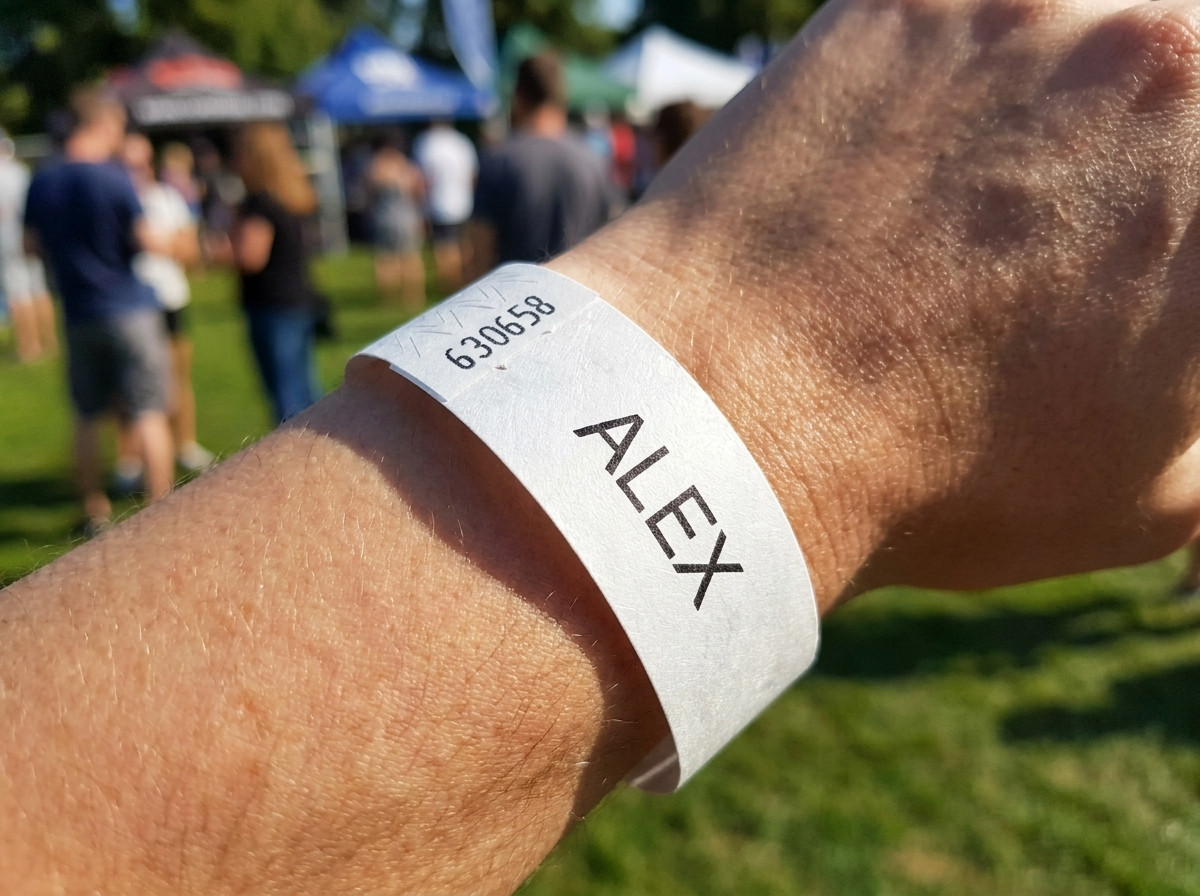 Vitt Tyvek-armband tryckt med ett barns förnamn och ett nödtelefonnummer, buret på handleden av ett litet barn vid ett utomhousevenemang